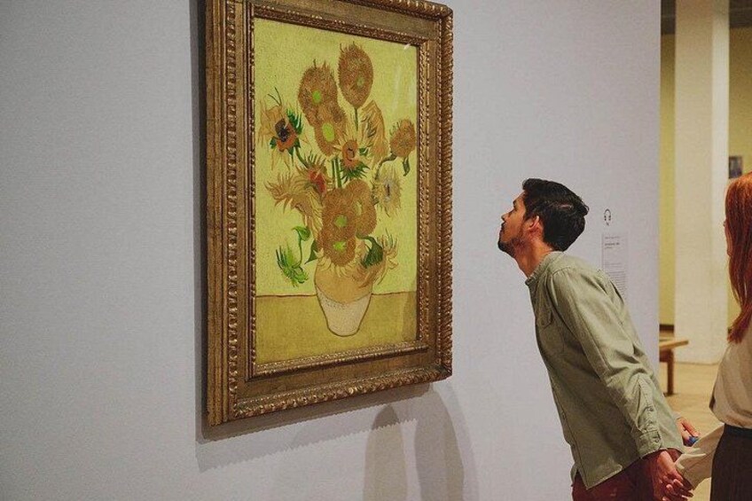 Une personne est en train de regarder un tableau encadré représentant des tournesols, qui est accroché à un mur. 2