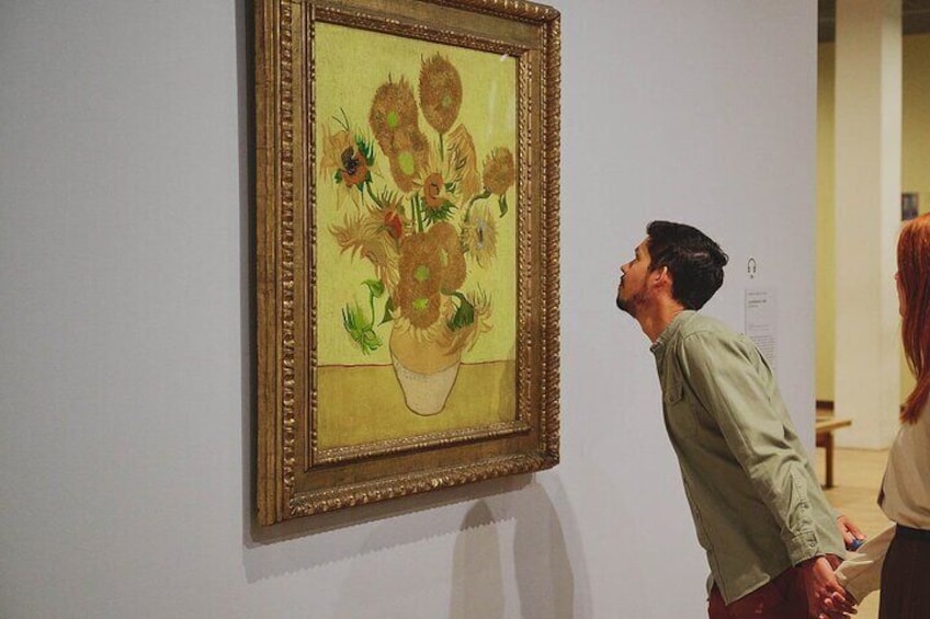 A person looking at a framed painting of sunflowers on a wall. 3