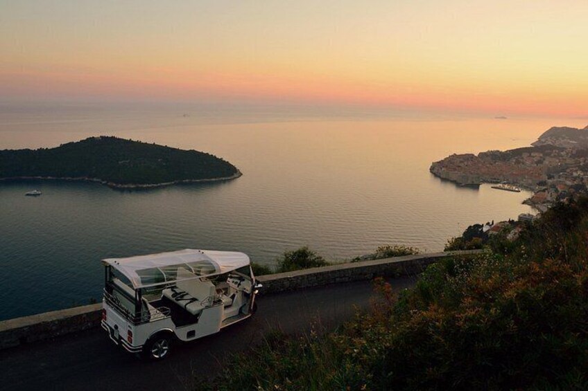 A white bus parked on a coastal road with a view of the sea and a small island. 4