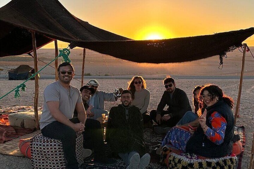A group of people sitting under a tent at sunset on a desert landscape. 4