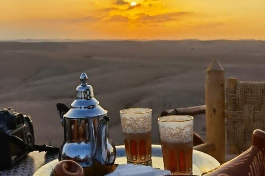 Paisaje desértico con atardecer, una tetera y dos tazas de té sobre una mesa. 2