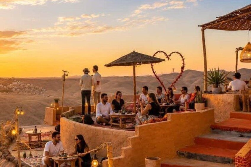 Un grupo de personas cenando al aire libre, con un paisaje desértico de fondo. 3