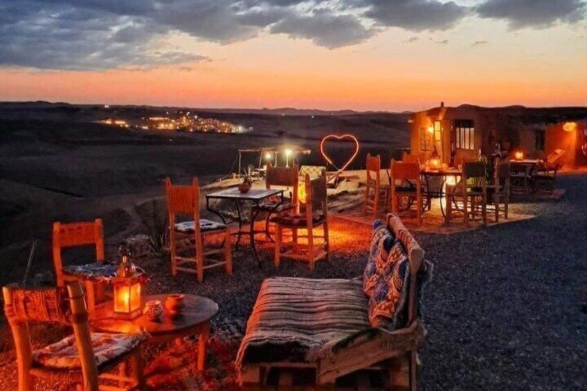 A desert landscape at dusk with a rustic outdoor seating area and a small building with lights. 3