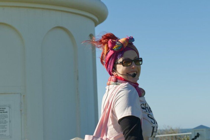 A person with colorful hair and a pink scarf standing in front of a white structure with arched windows. 4