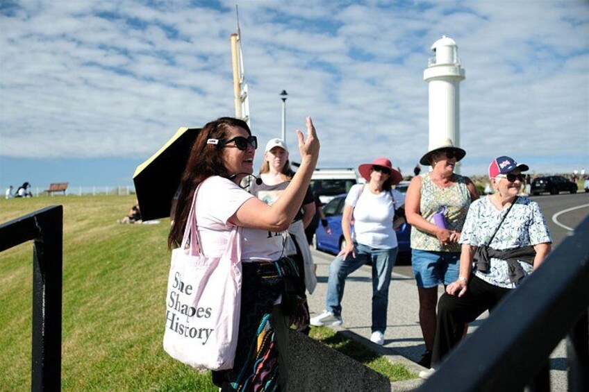 A group of people at a coastal location with a lighthouse in the background. 2
