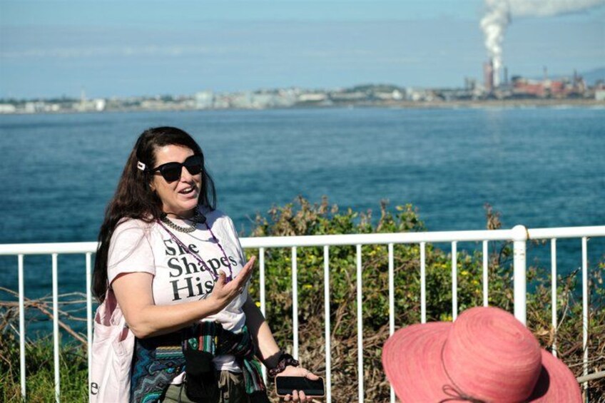 A person sitting on a railing by a body of water, wearing a t-shirt with text, and a pink hat. 5