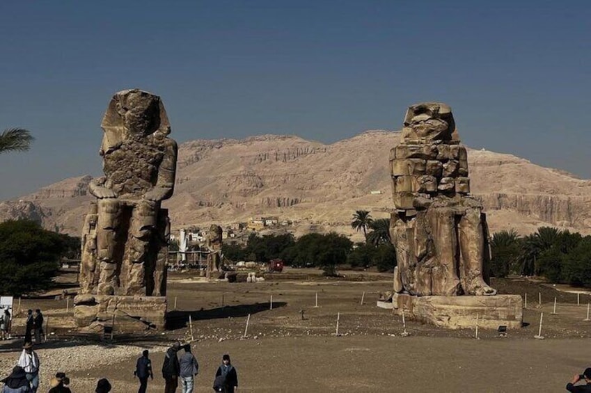 Deux grandes statues de pierre se dressent dans un paysage désertique, avec des montagnes en arrière-plan. 3