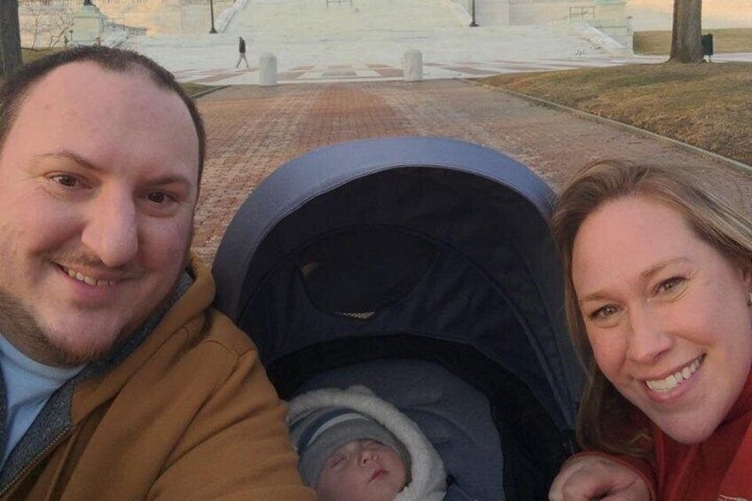 A stroller with a baby, a person in a brown jacket, and another person in a red jacket. 2