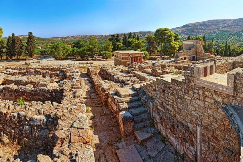 Ruinas antiguas con muros y escalones de piedra, rodeadas de árboles y un cielo despejado. 2