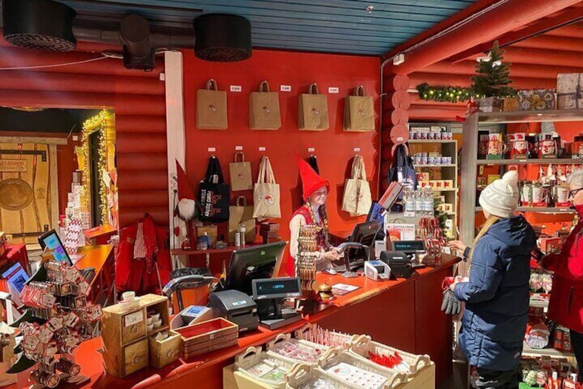 Ein festlich dekorierter Marktstand mit rotem Innenraum, geschmückt mit Weihnachtsdekoration, und einer Theke, an der ein Kunde bedient wird. 4