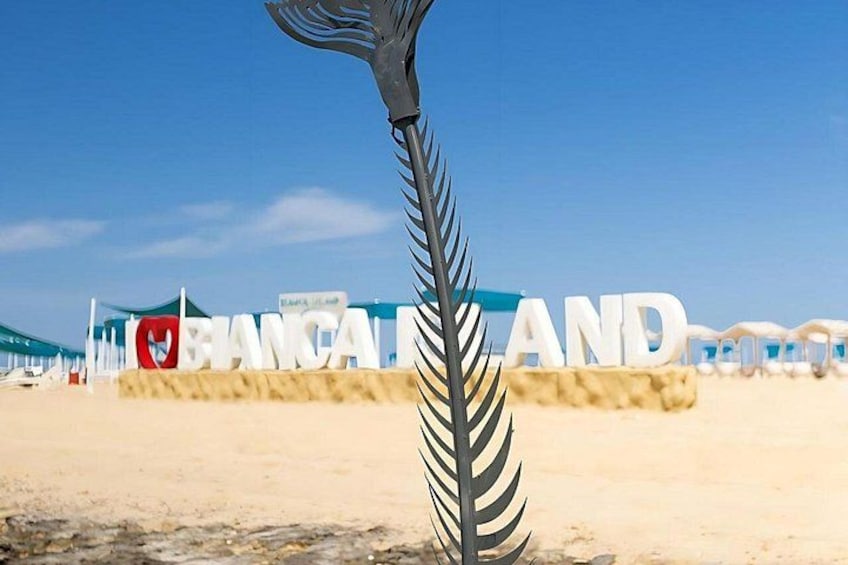 Une plage avec un panneau sur lequel on peut lire « BIANCA ET… » et une sculpture métallique décorative. 5