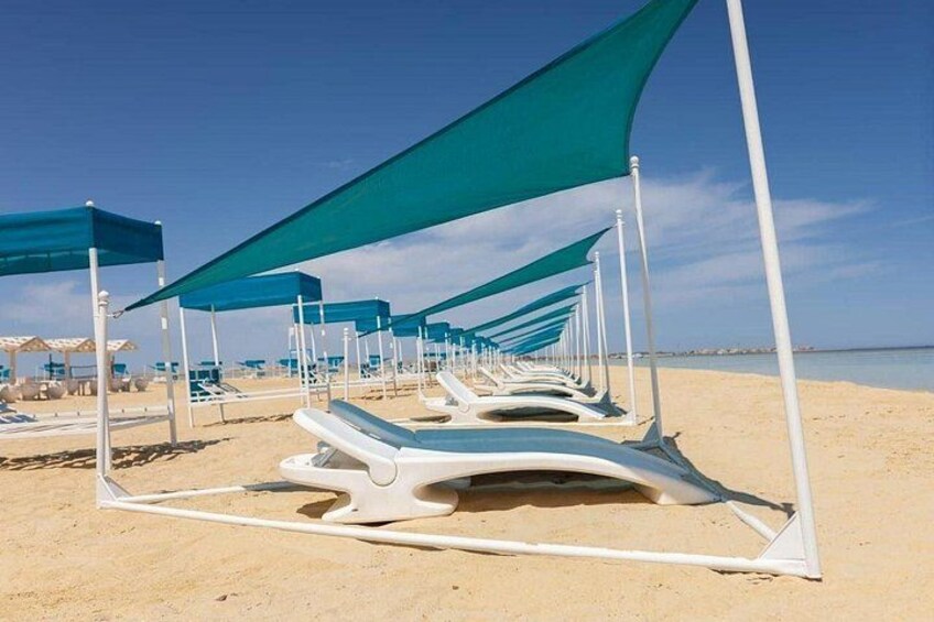 Une rangée de chaises longues dotées de toiles vertes, sur une plage de sable. 3