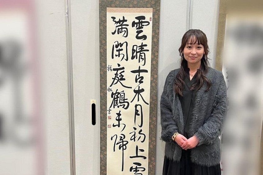 A person standing in front of a wall with a vertical sign containing Japanese text. 5