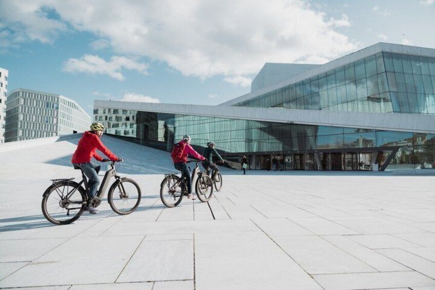Drei Radfahrer auf einer befestigten Fläche vor einem modernen Glasgebäude. 1