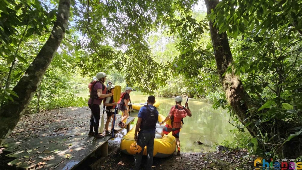 People preparing to raft on a calm river surrounded by dense forest. 2