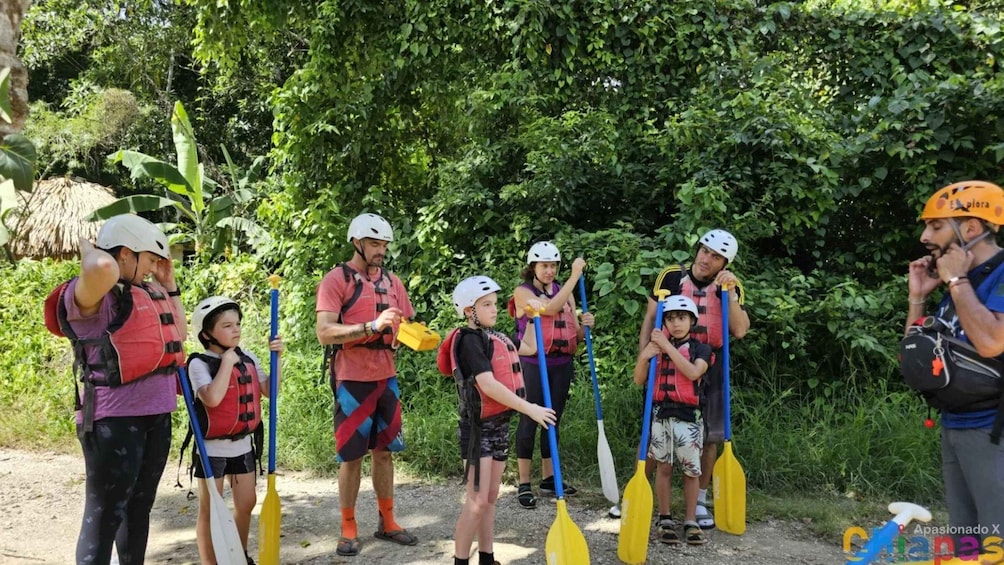 A group of people preparing for a kayaking activity, wearing life jackets and helmets, with a lush green background. 3