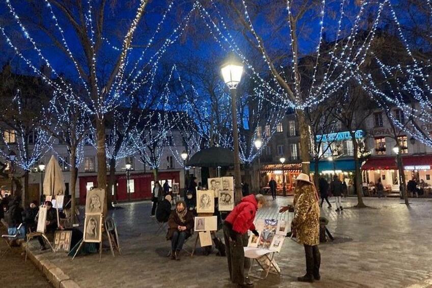 Une exposition d’art en plein air, avec des arbres décorés de guirlandes lumineuses, une rue bordée de boutiques et des passants. 3