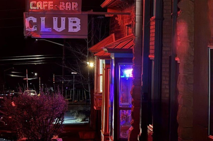 A nighttime view of a building with a neon sign reading 'CAFE BAR CLUB' and a lit entrance. 3