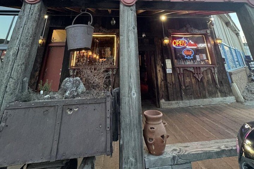 Un edificio rústico de madera con un letrero de neón, un balde de metal y una maceta de barro. 2