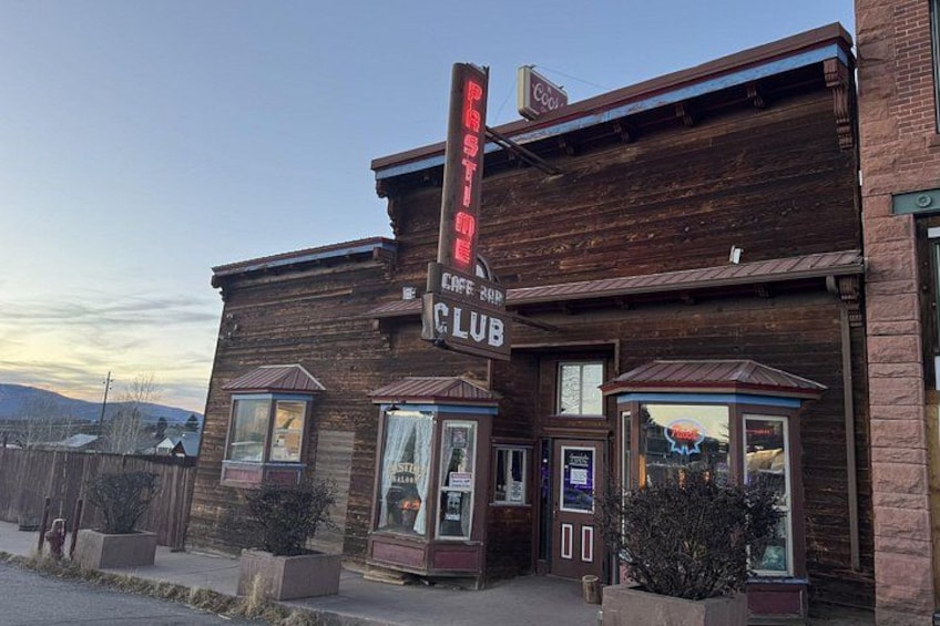 A wooden building with a neon sign, windows, and a door. 1