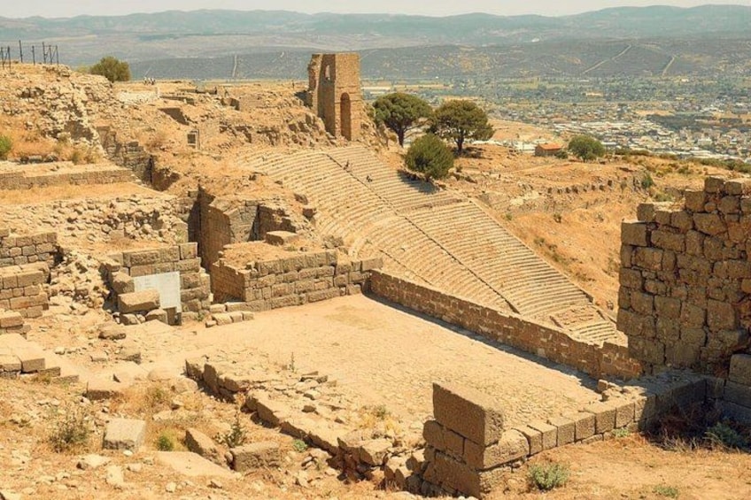 Ancient ruins with a partially intact amphitheater, stone walls, and a distant view of a city. 2