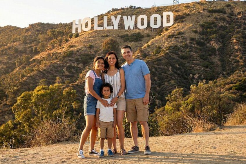 En familie står foran Hollywood-skiltet med et bakket landskab i baggrunden. 1