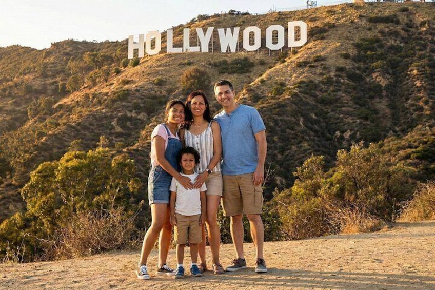 Eine Familie steht vor dem Hollywood-Schild mit einer hügeligen Landschaft im Hintergrund. 1