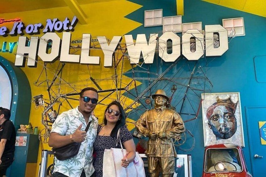 A couple posing in front of a 'HOLLYWOOD' sign with a statue and a painting. 3