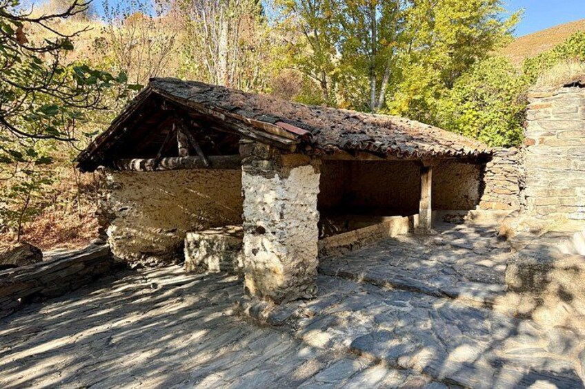 A rustic stone building with a tiled roof, surrounded by trees and a stone wall. 3