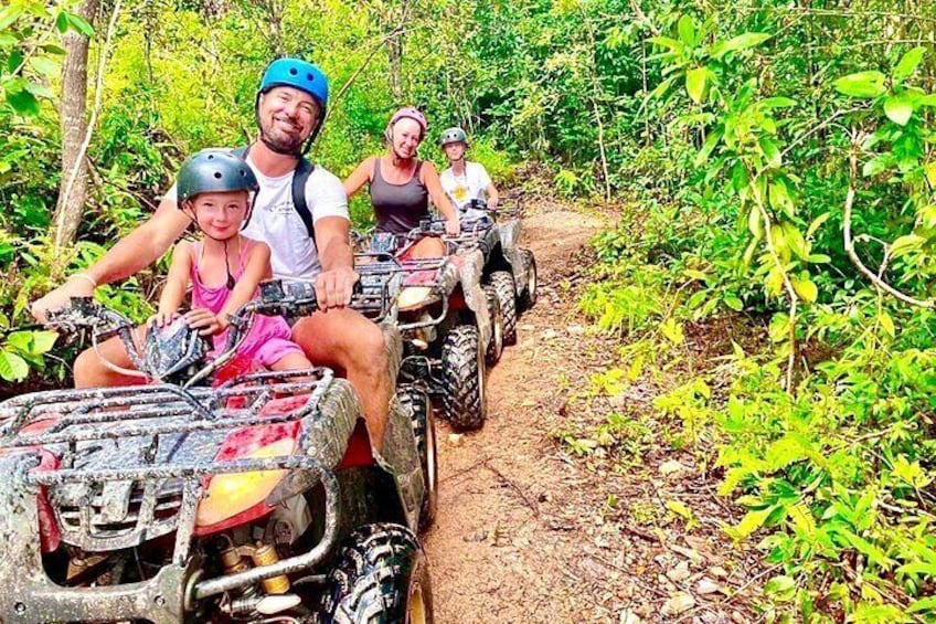 Four people on ATVs on a dirt path surrounded by greenery. 2