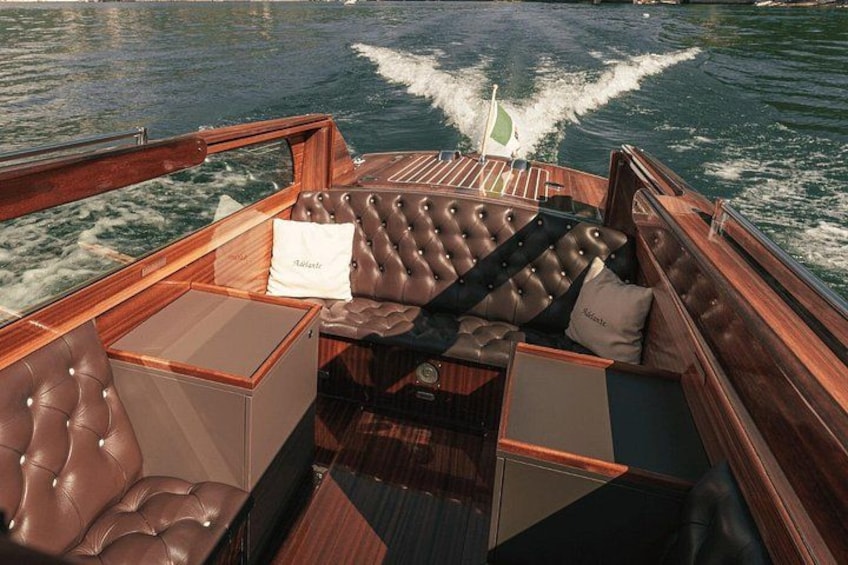 A boat's deck with leather seating, a steering wheel, and a wake behind the vessel. 5