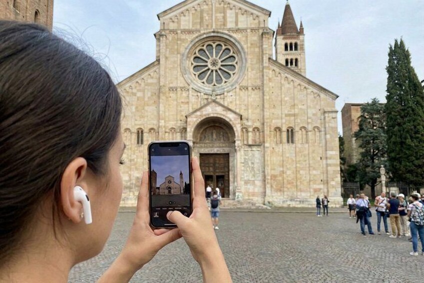 A person taking a photo of a historic building with a large circular window and a clock tower. 4