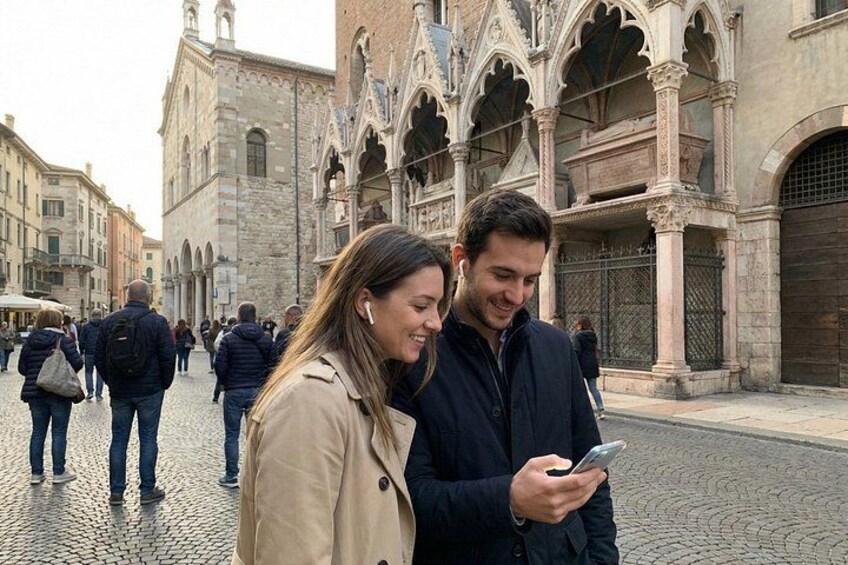 A couple looking at a smartphone in a historic square with stone buildings. 2