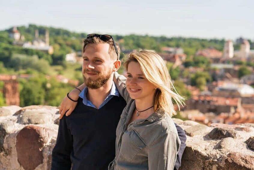 Dos personas sobre un muro de piedra, con un paisaje urbano de fondo. 2
