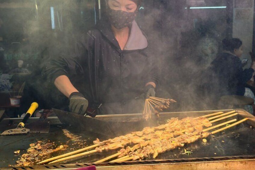 Eine Person bereitet Spieße auf einem Grill zu, Rauch steigt auf. 5