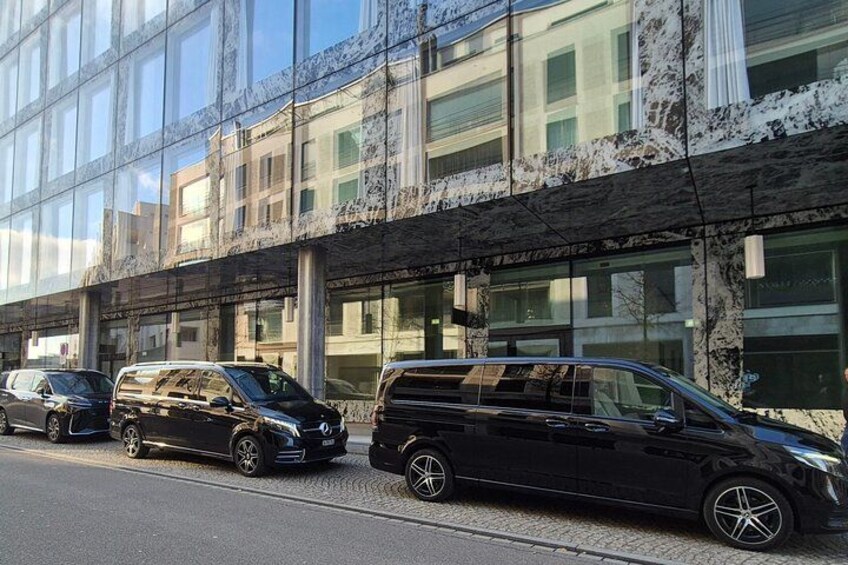 Een zwarte minibus geparkeerd voor een modern gebouw met reflecterende glazen ramen en een marmeren gevel. 3