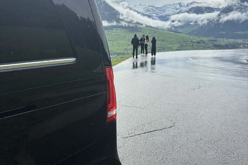 Un véhicule noir est garé sur une route mouillée, et un groupe de personnes se tient à distance. 2