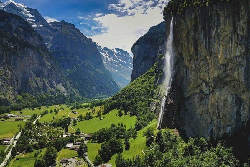 Een bergachtig landschap met een waterval, weelderige groene valleien en een klein dorp. 5