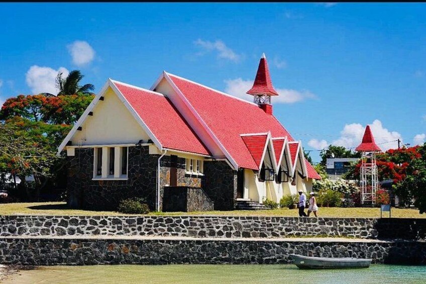 A building with a red roof and stone walls, a boat in the water, and a clear blue sky. 1