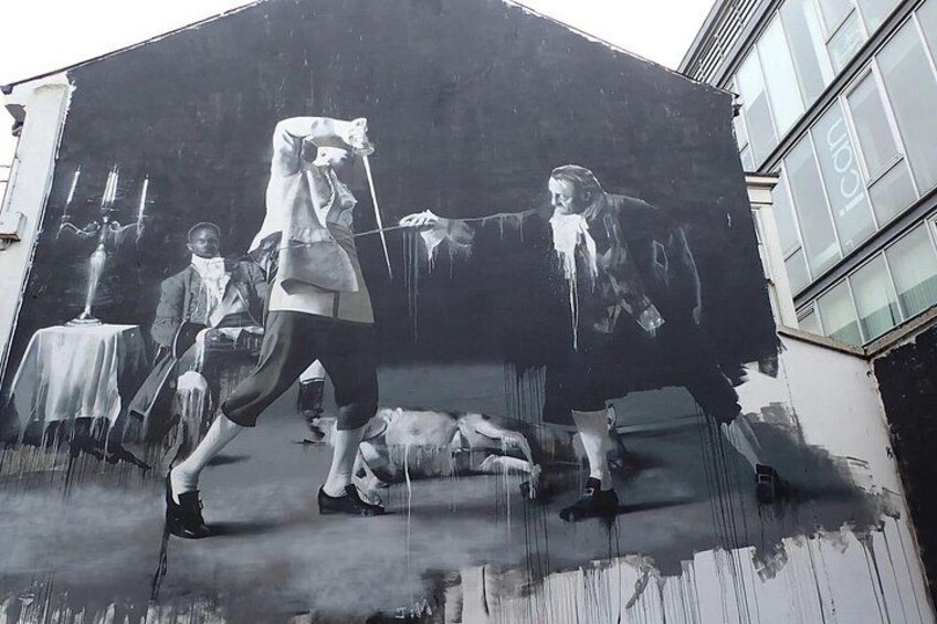 A mural on a building with a person in a suit and tie, another person lying down, and a third person in the background. 3