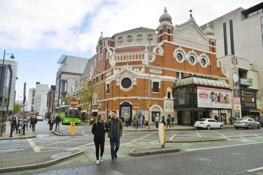 A busy urban street with pedestrians, a bus, and a historic building with ornate architecture. 2