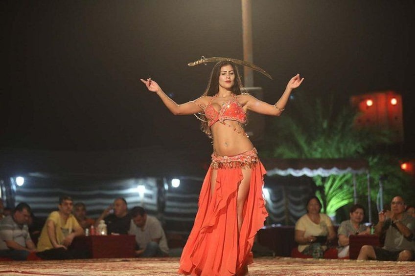 A person performing a dance on a stage with an audience seated in the background. 2
