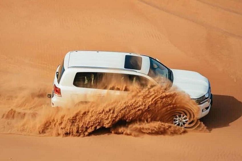 A white SUV driving through a desert, kicking up sand. 5