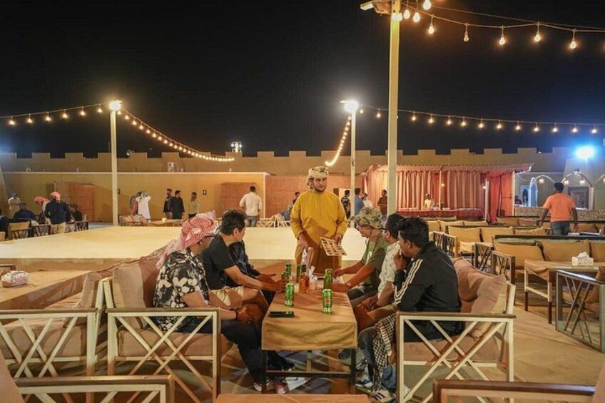 An outdoor gathering with people seated on couches and chairs, under string lights. 3