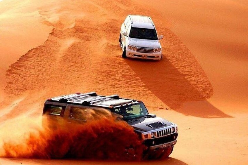 A white off-road vehicle driving through a desert with sand dunes. 1
