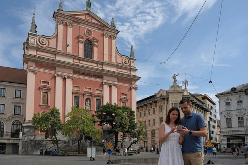 A couple standing in front of a pink church with a statue in the background. 5