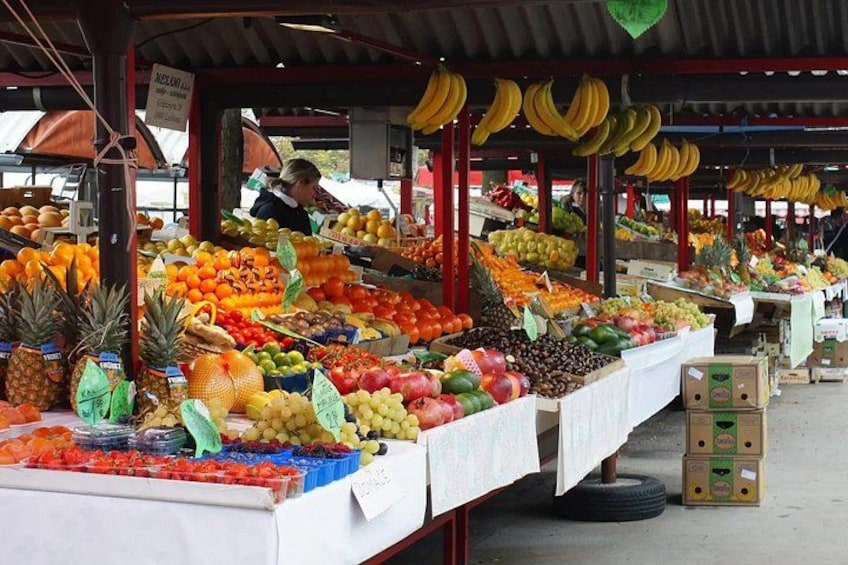 A fruit market with various fruits displayed on tables and hanging from the ceiling. 2