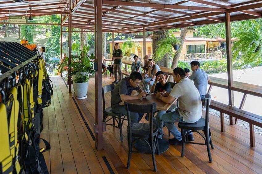 Een overdekt terras met tafels en stoelen, omgeven door potplanten en een houten terras. 3