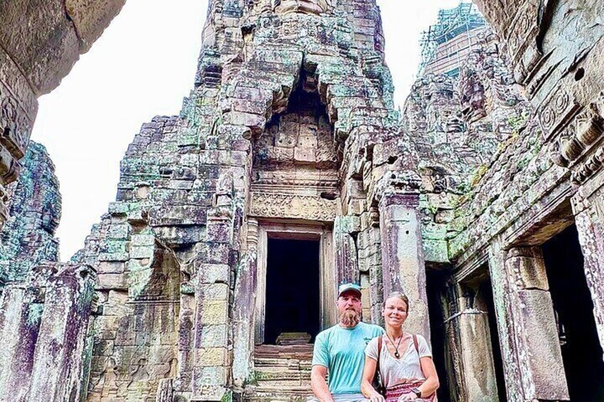 A man and a woman standing in front of an ancient stone structure with intricate carvings and a doorway. 3