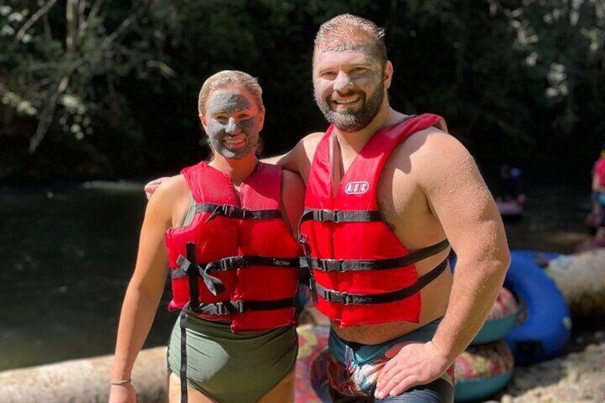 Two people wearing red life jackets standing near a body of water with trees in the background. 5